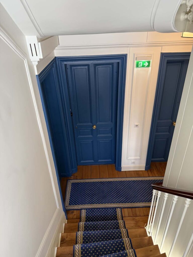 Vue d'ensemble cage d'escalier : Porte et tapis bleu